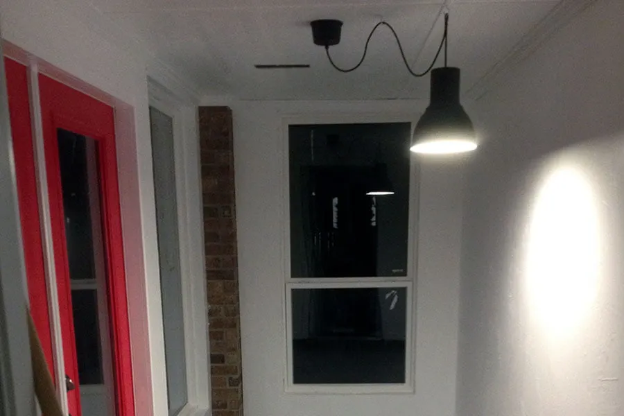 The inside of the new studio at night. A black lamp hangs from the white ceiling. The double backdoor is painted red. 