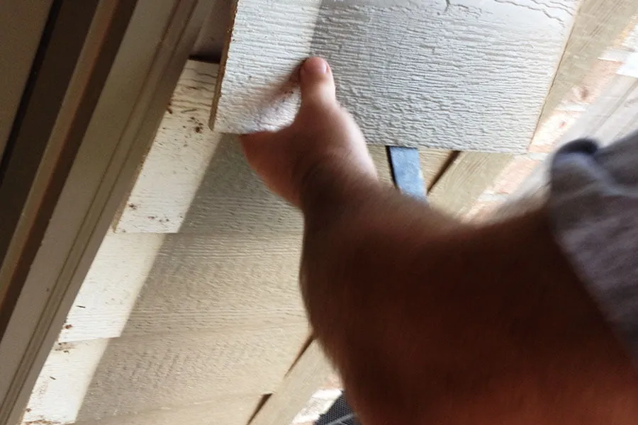 A man removes layers of siding from the house's exterior at the beginning of studio construction. 