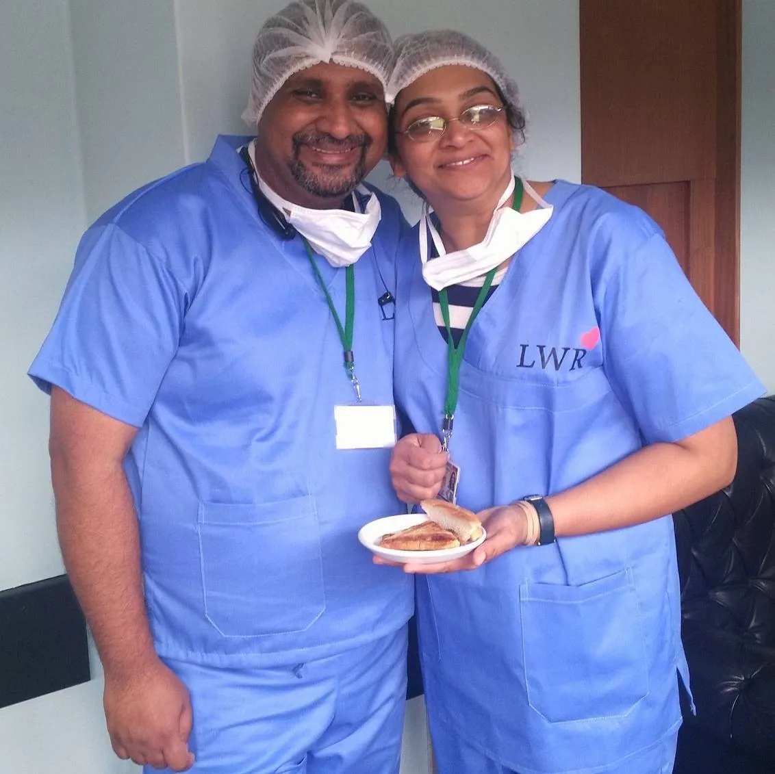 Susan and Santhosh, leaders of Love Without Reason, smile together. Both are wearing surgical scrubs. 