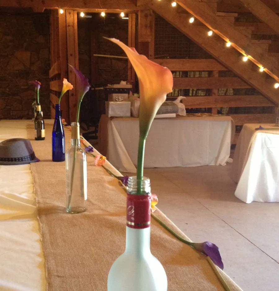 The table layout at the Thompson wedding. Different wine bottles are the centerpieces, each with either an orange or purple tulip. 