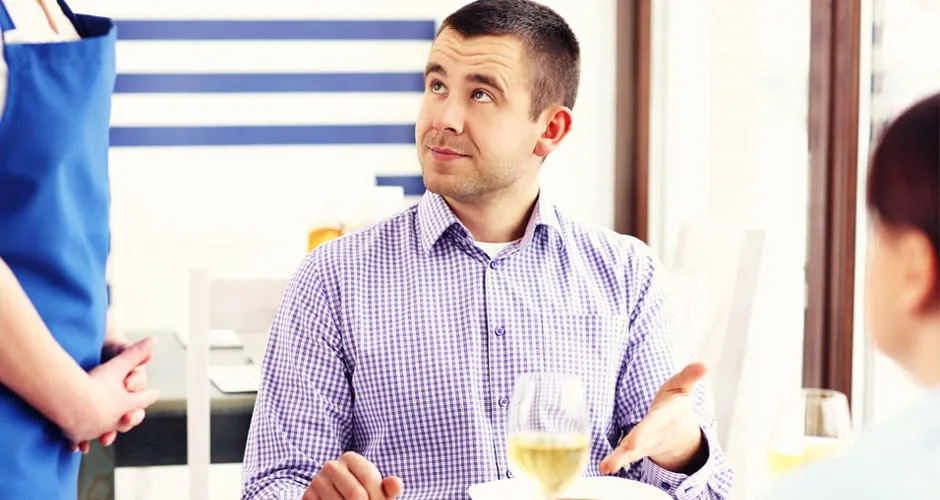 A man talks to a server at a restaurant table. He is not satisfied with his order. 