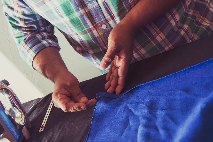 Sam sews together blue and black pieces of fabric with a needle and thread. 