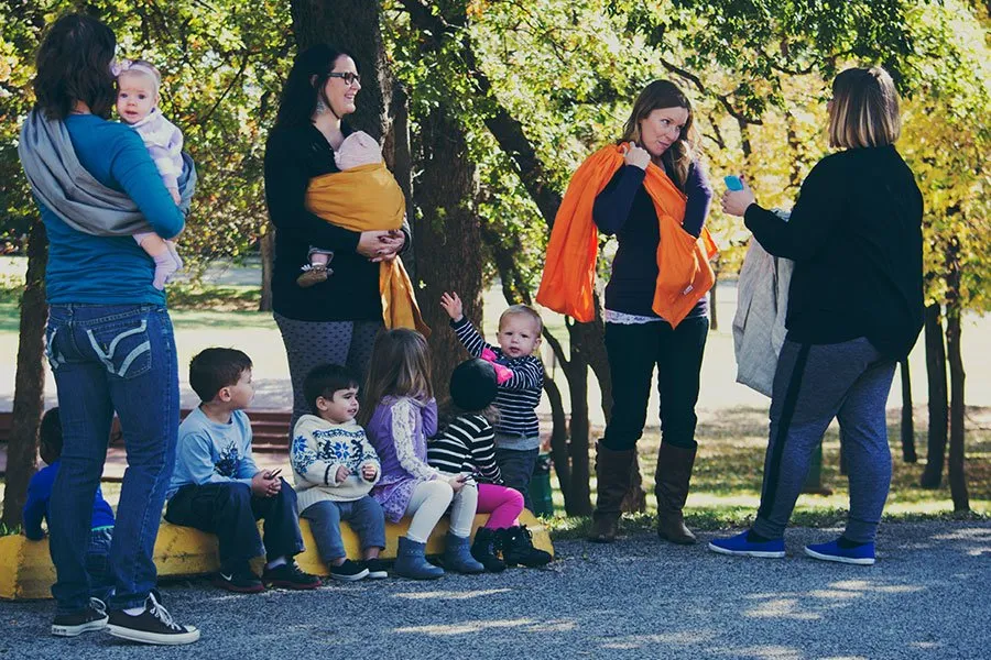 Amy talks to a group of moms about how to use the SlingRing. A group of small children sit below at their feet. 