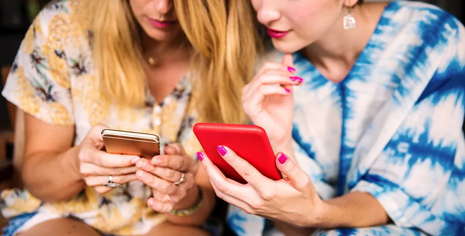 Two women hold their smartphones while reading engaging content created by Oklahoma SEO services. 
