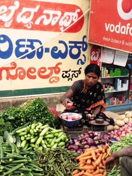An Indian woman cuts onions while at a market. 