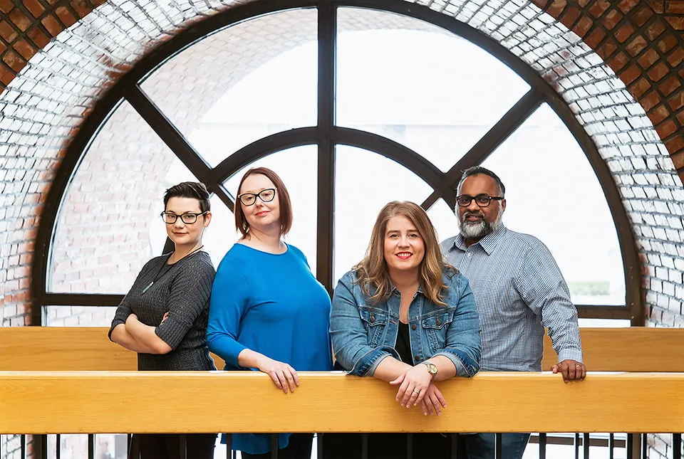 The myheartcreative team of four people, Sam, Amy, April, and Morgan, stand in front of a large window. 