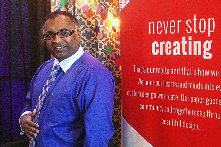 Sam wears a purple button-up and matching plaid tie while standing in front of the retractable banner. 
