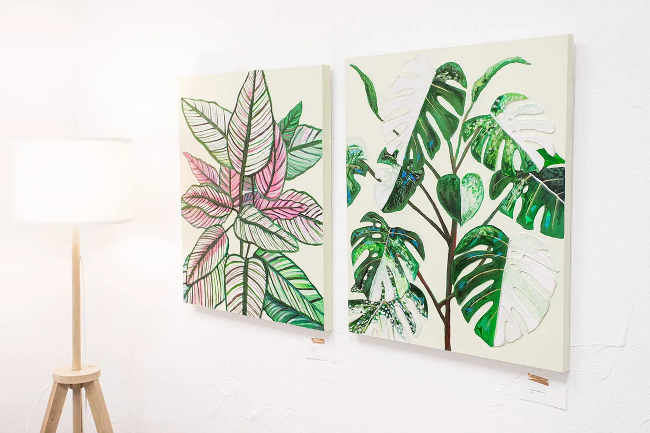 Two paintings of houseplants hang on the wall in the design studio next to a lamp. The paintings are painted by OKC Featured Artist Kyndall Rainey. 