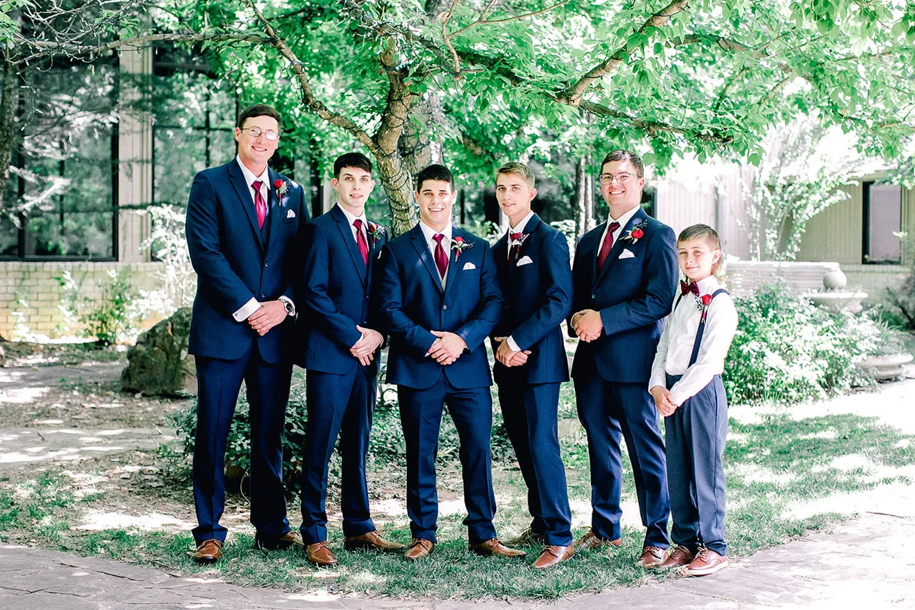 Derek and Shelby Thunderbird Chapel Wedding - myheartcreative The groom and four groomsmen smile for a photo while wearing navy suits with maroon ties. A junior groomsmen stands on the far right side wearing a white button down, maroon bow tie, and suspenders.