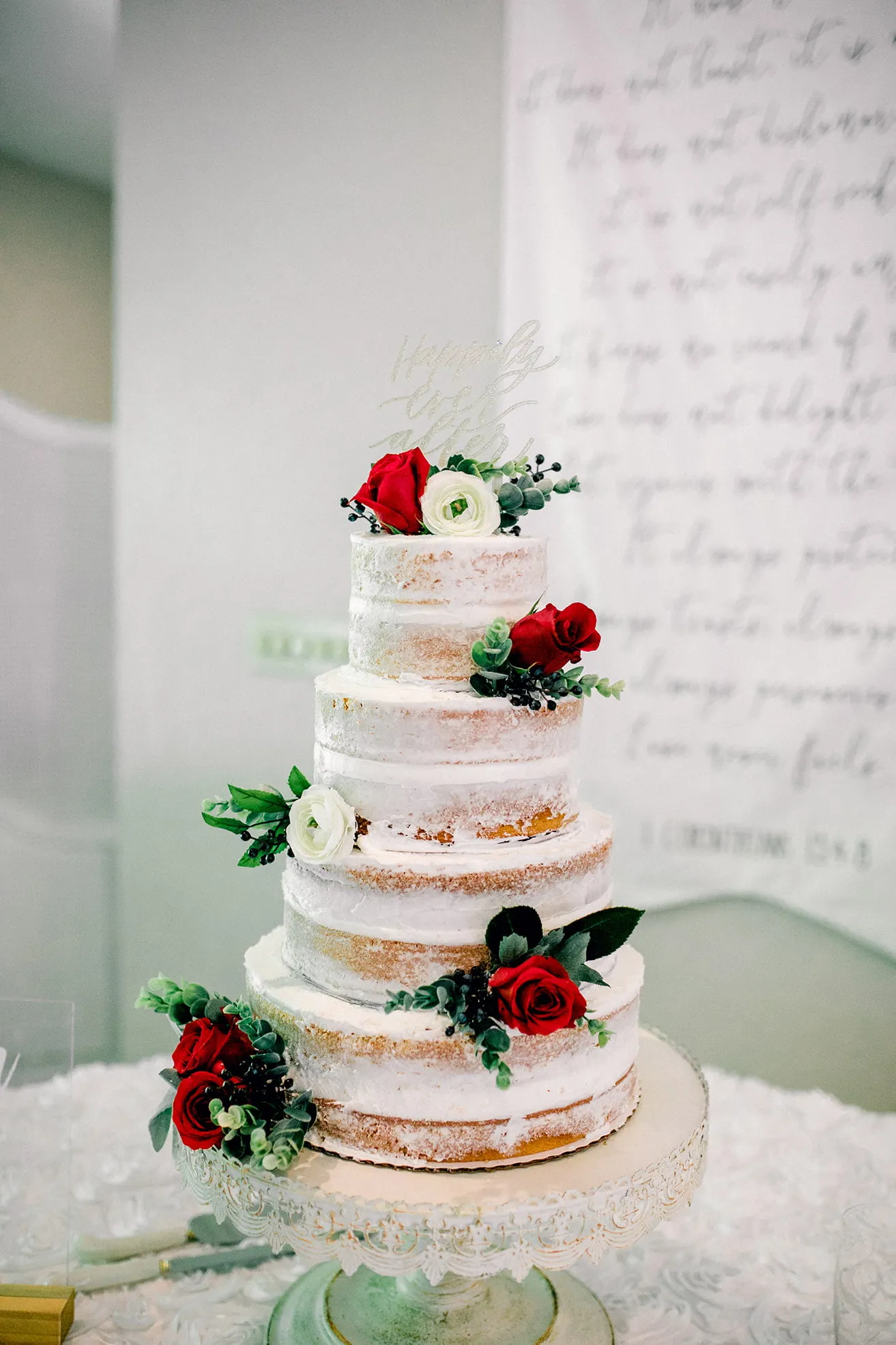 Derek and Shelby Thunderbird Chapel Wedding - myheartcreative Derek and Shelby's wedding cake. It is a four-tiered cake with white frosting, maroon and white flowers, and a cake topper that says, "Happily Ever After".
