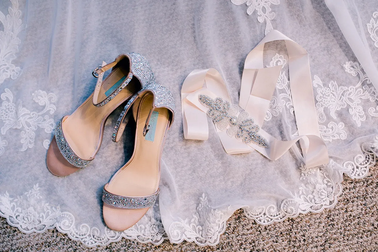 Jeff and Kasey The Palace Wedding - myheartcreative A pair of sparkly, strappy heels is photographed on the lace train of the wedding dress. The bride's white satin belt with beaded applique rests next to it.