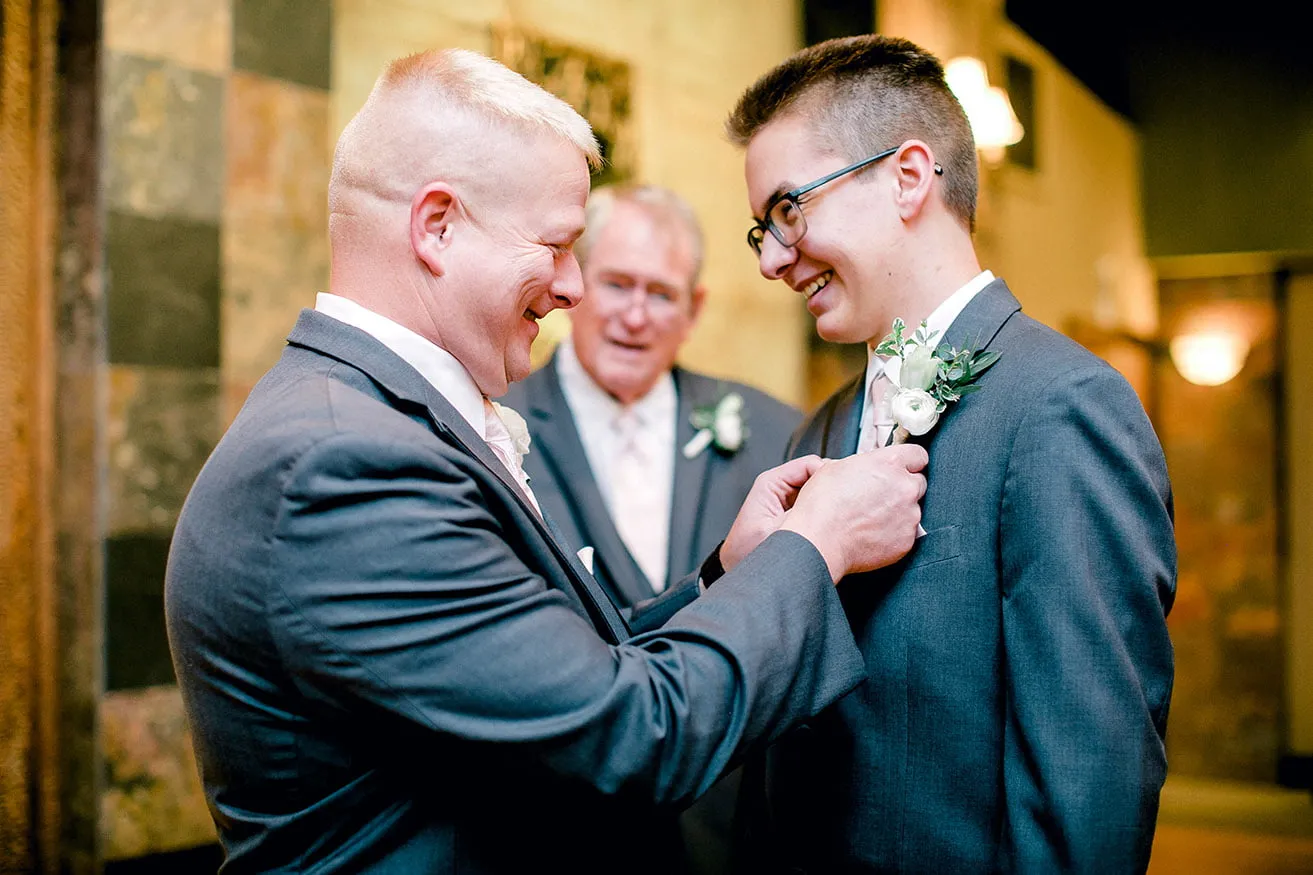 Jeff and Kasey The Palace Wedding - myheartcreative The groom pins a boutonniere on his son's suit jacket while the groom's father looks on.