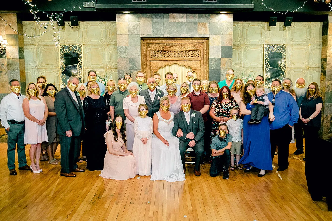 Jeff and Kasey The Palace Wedding - myheartcreative The bride and groom pose for a large family photo after their ceremony. Everyone is wearing gold face masks.