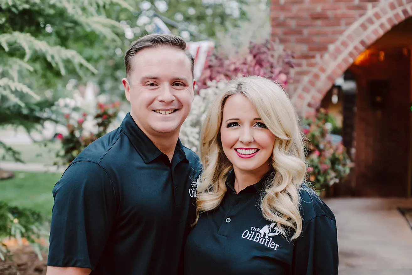 The two owners of The Oil Butler smile together for their commercial photography OKC session. They are wearing matching black polos with the company logo embroidered in the corner. 