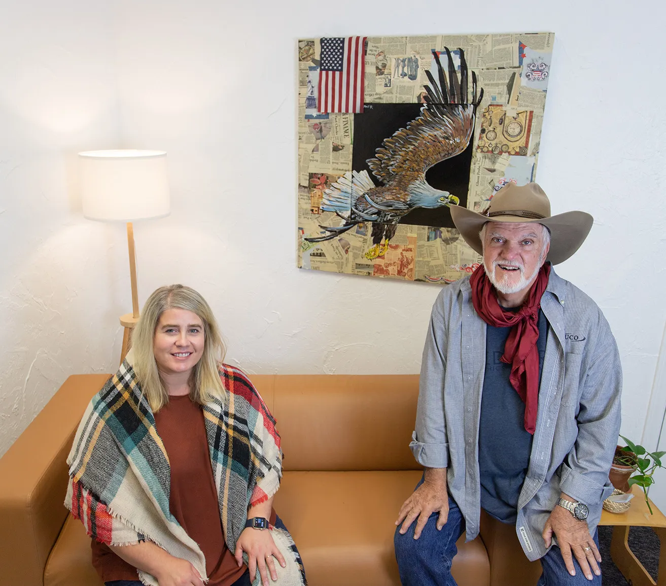 Dr. Bob Palmer and Amy Samuel sit together and pose for a photo on a couch at the myheartcreative studio. One of Palmer's artworks hangs on the wall behind the couch. 