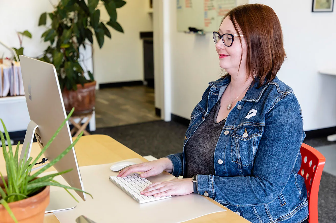 April sits at her desk and types out client content on her desktop. 