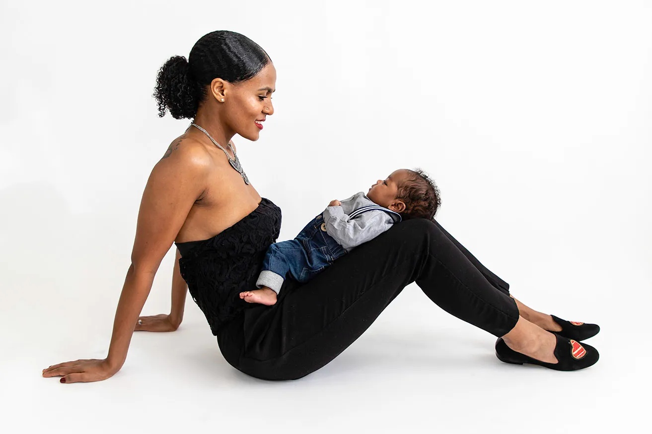 A mother smiles at her baby boy while he rests on her bent legs during a newborn photoshoot OKC. 