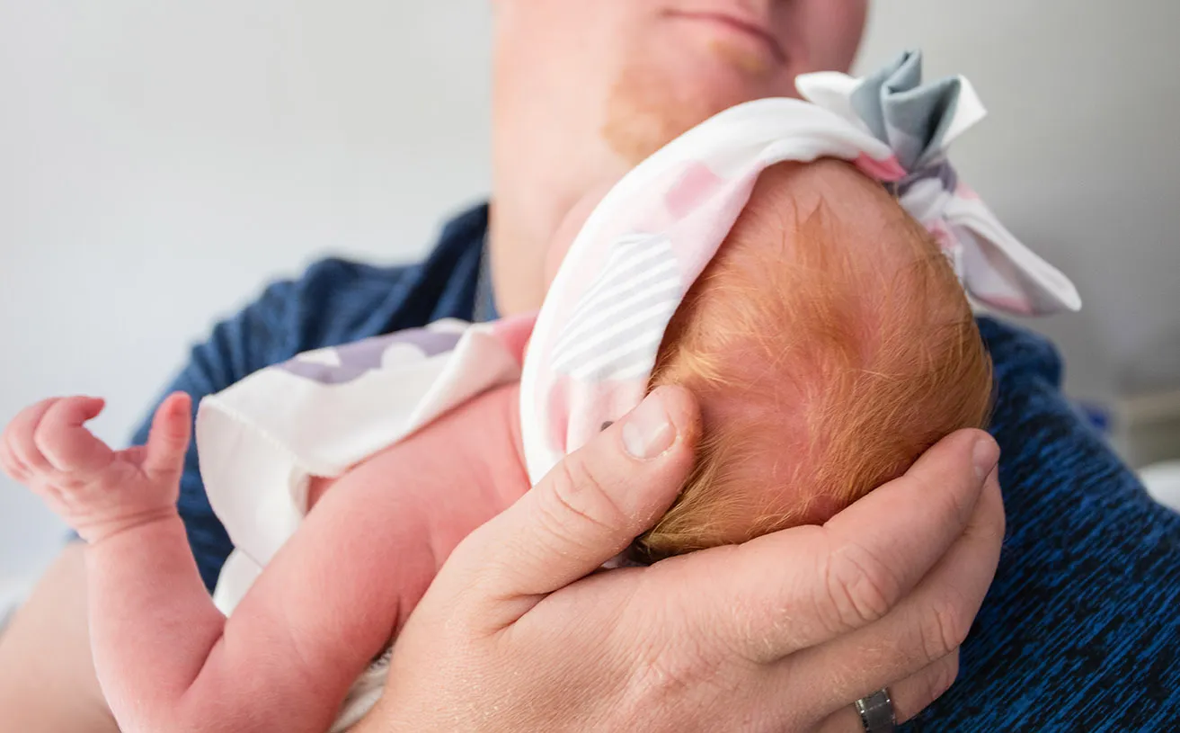 A new father gradles his daughter's head during a newborn photography session. 