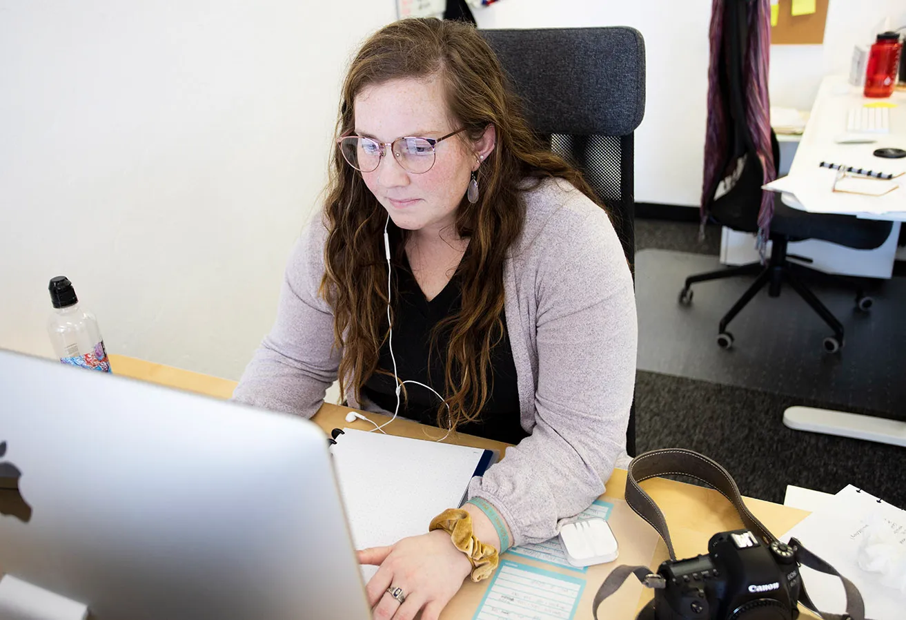 Morgan sits at her desk in the studio and works on writing content for client websites. She is listening to music with headphones as she works. 