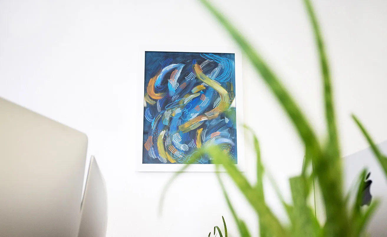 An abstract blue painting from artist Chandler Domingos hands between two desks at the studio. 