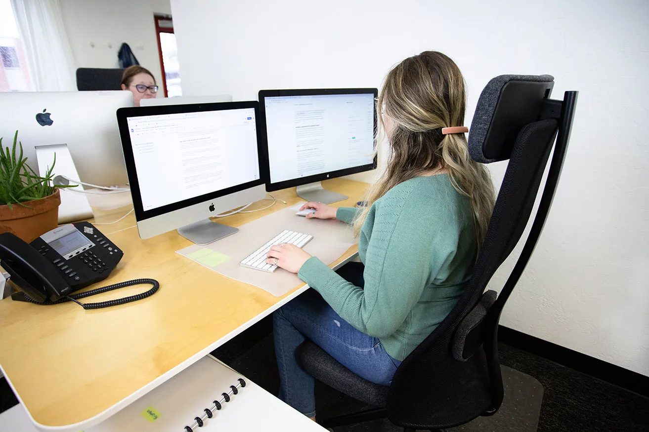 Kristen writes content for a client on her desktop computer at her desk, while sitting across from April at the studio. 