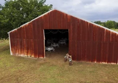A large red rustic barn with a wedding ceremony set up inside.