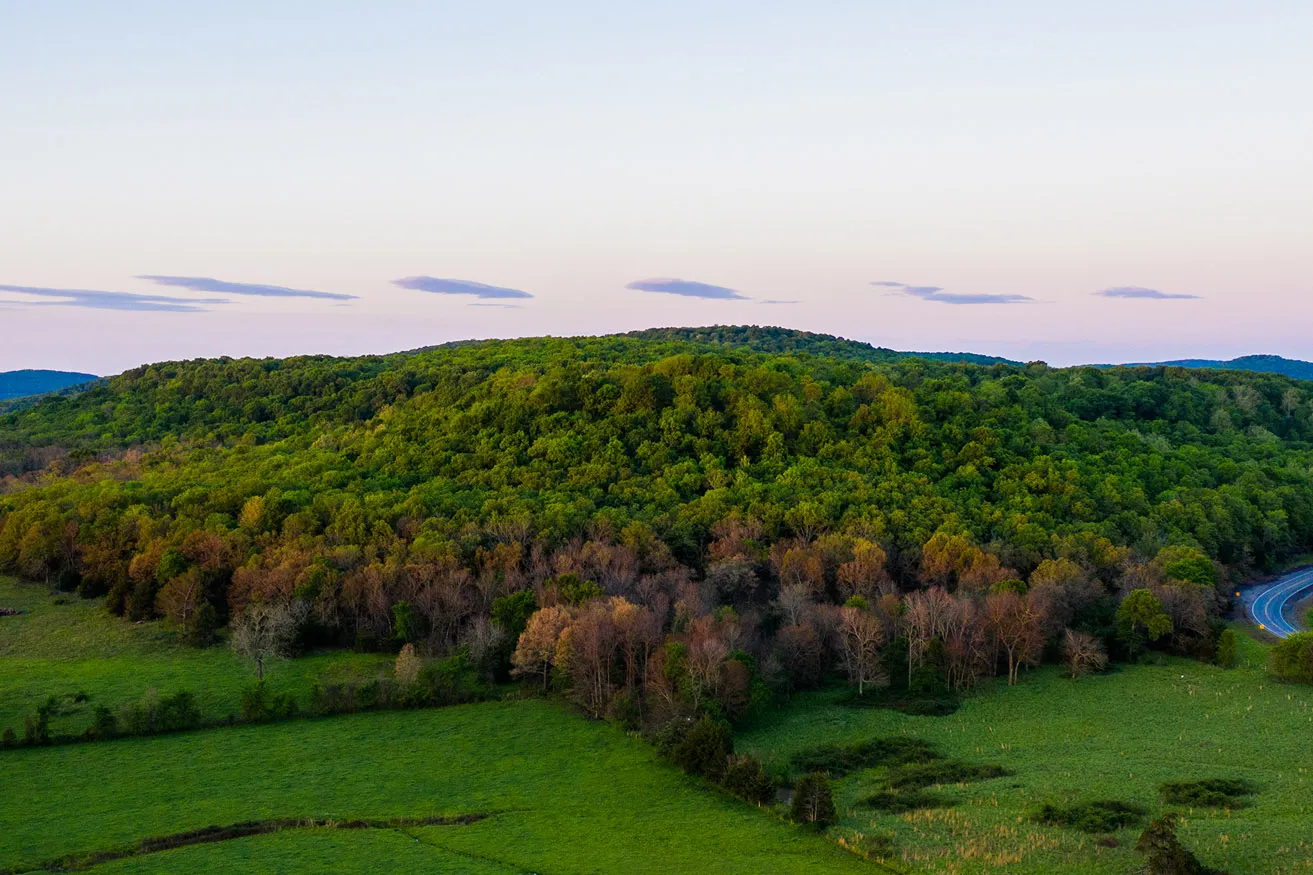An aerial photograph of a tree-covered hill in the Oklahoma countryside. 
