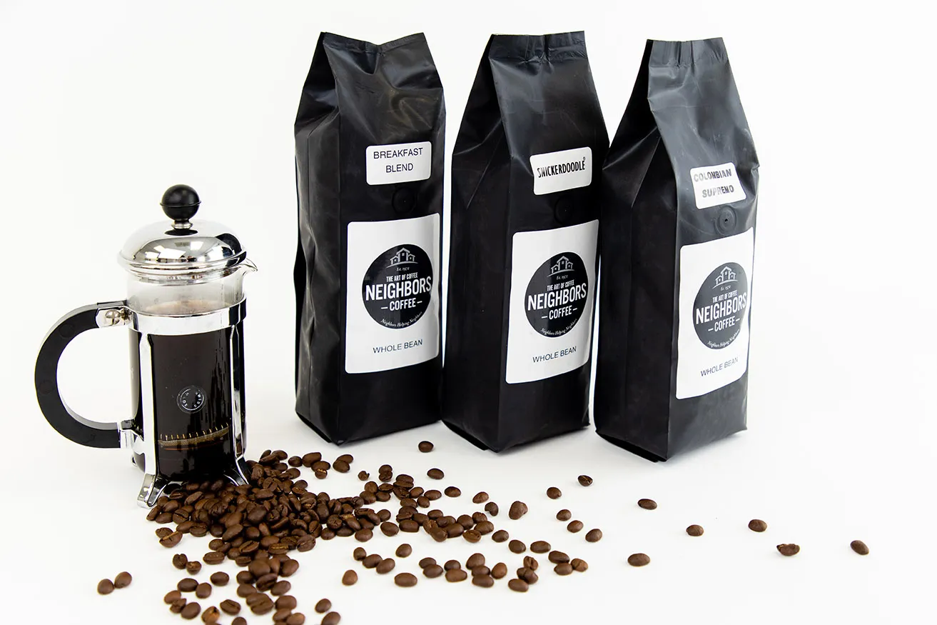 What Are the Benefits of Dallas Commercial Photography? - myheartcreative Professional Dallas Photography of three bags of Neighbor's Coffee on a white backdrop. The bags are sitting next to a french press filled with coffee and a pile of coffee beans scattered across the ground.