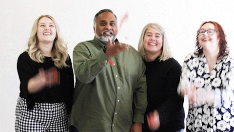 Kristen, Sam, Amy, and April throw red confetti in the air while standing in front of a white backdrop. 