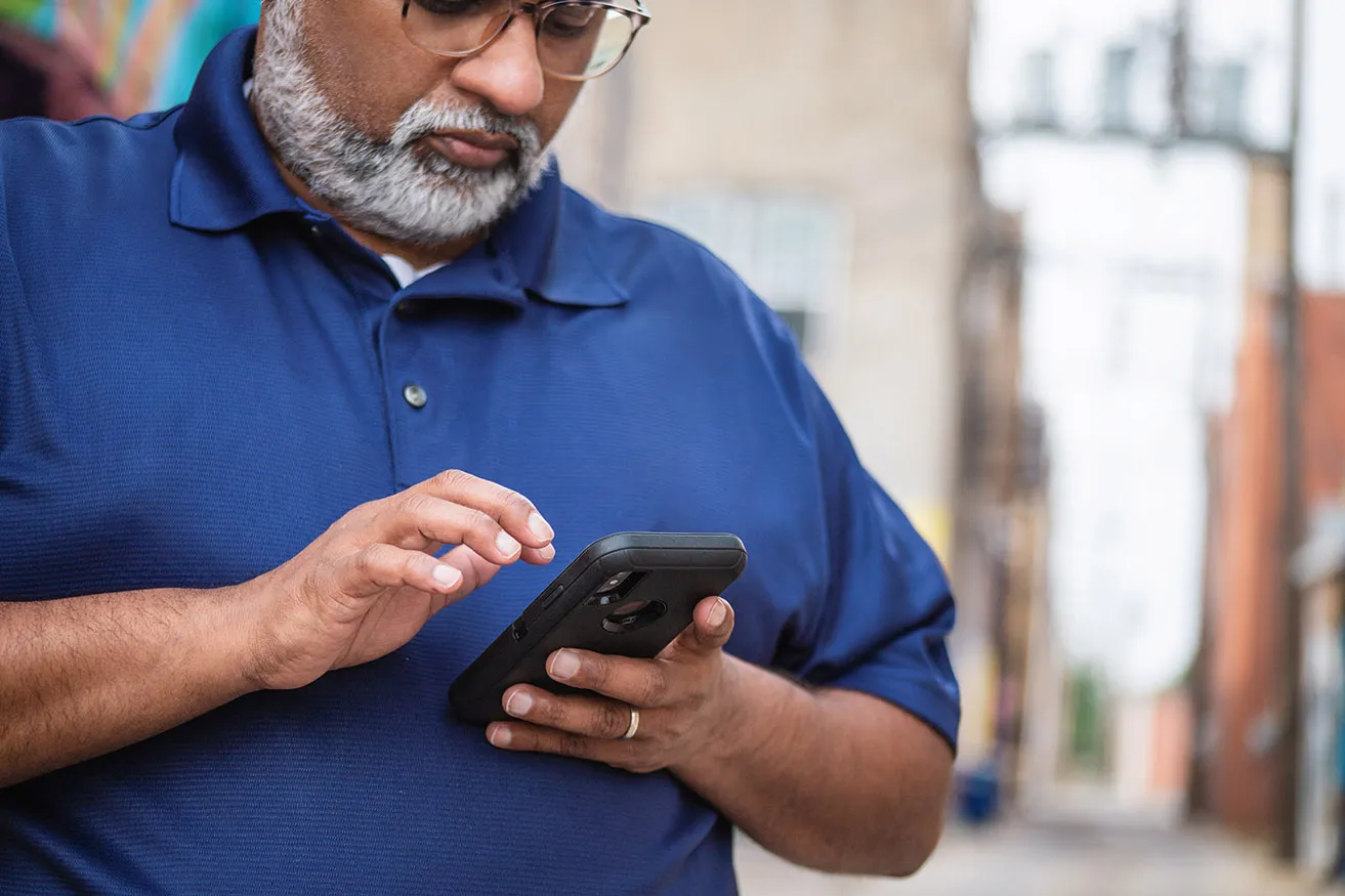 A man wearing a blue polo scrolls on social media on his smartphone. 