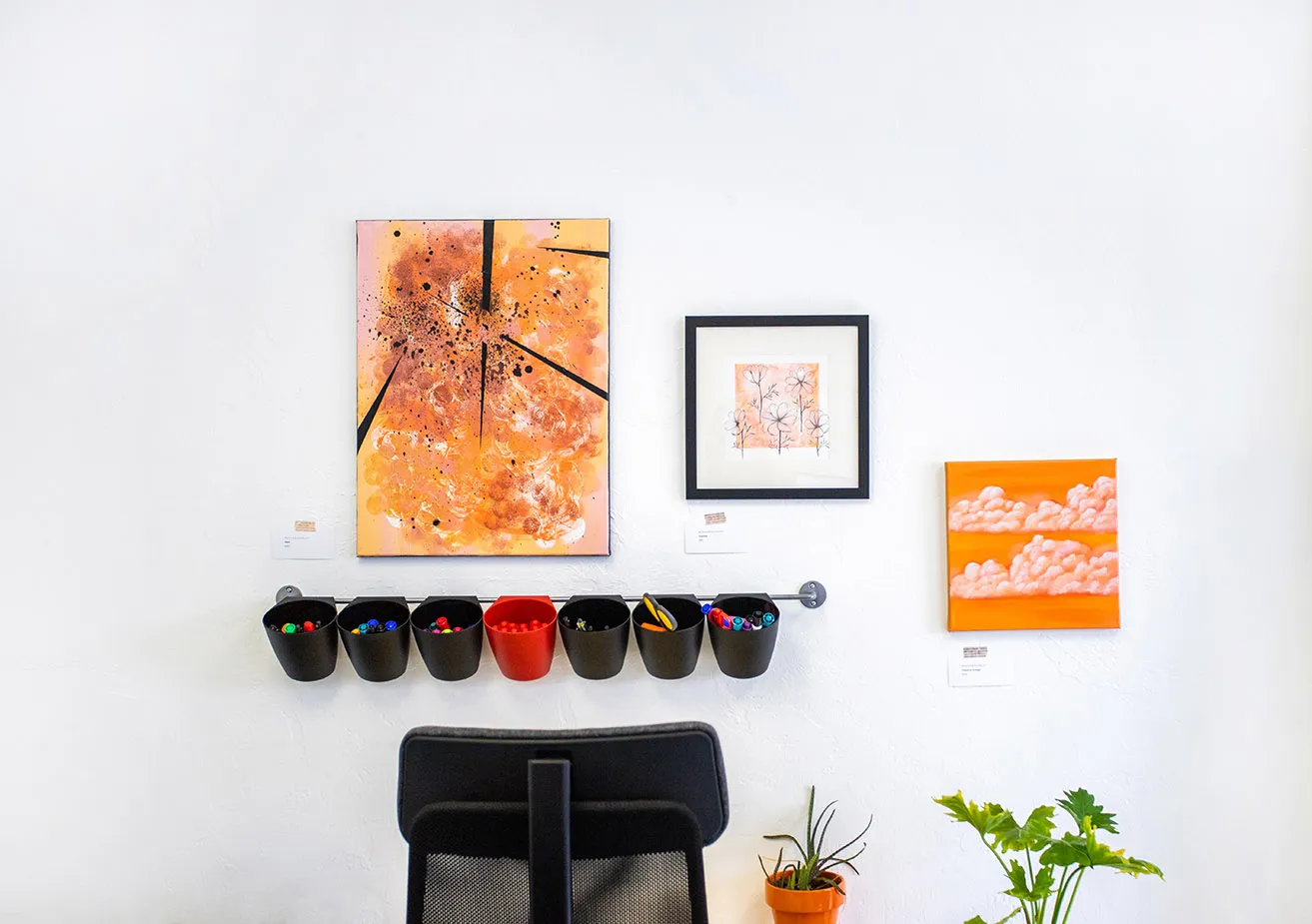 Three artworks by Reshon Shirley, all with orange color accents, hanging above a desk at the studio. 