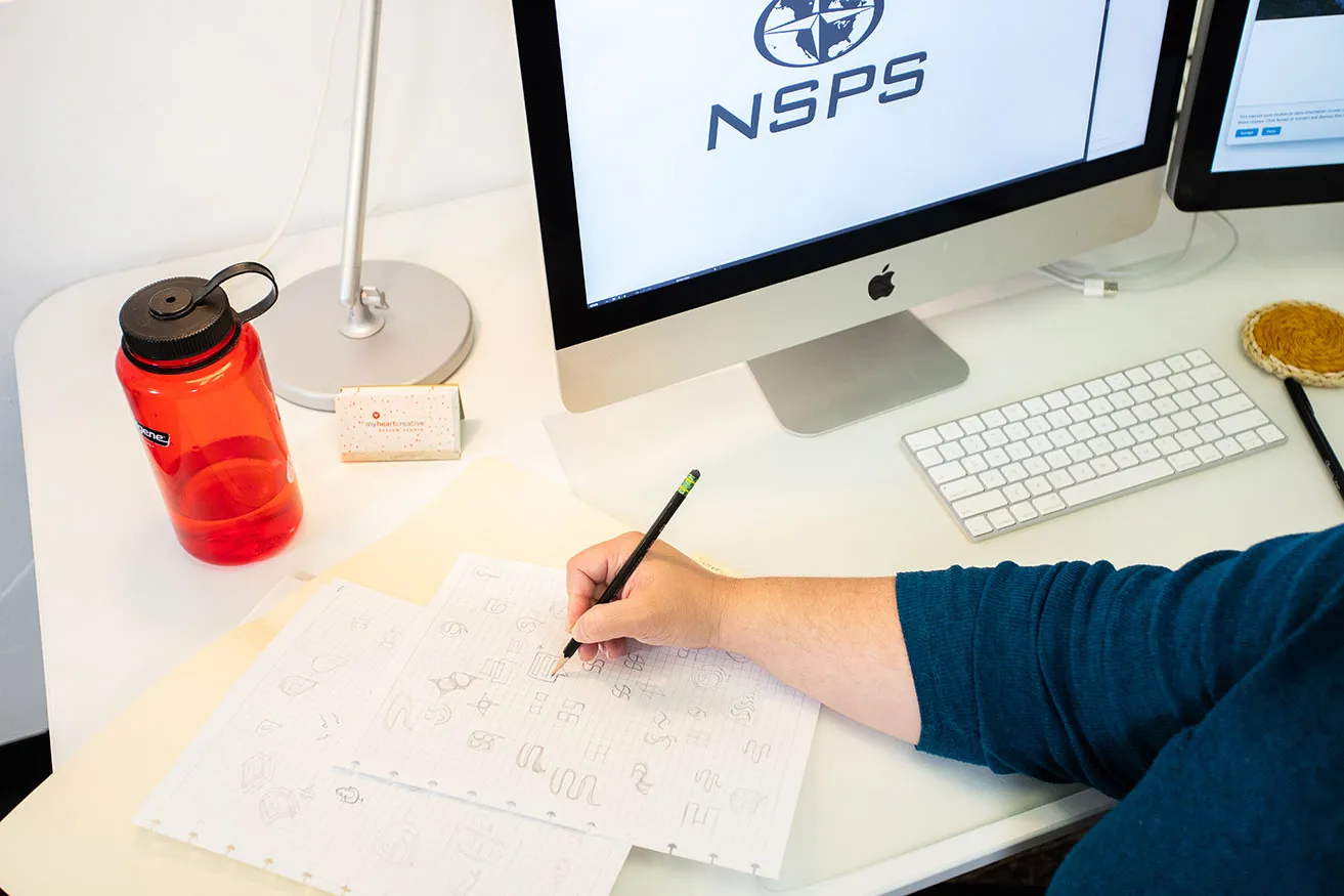 3 Steps to the Perfect Logo Design OKC Brief - myheartcreative An Oklahoma design professional uses a black pencil to sketch logo ideas for the new NSPS logo at her desk.