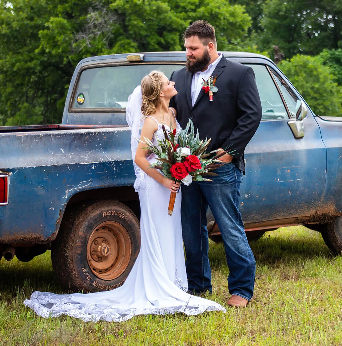 photography-wedding A bride and groom look at one another while being photographed in front of an old blue pickup truck.