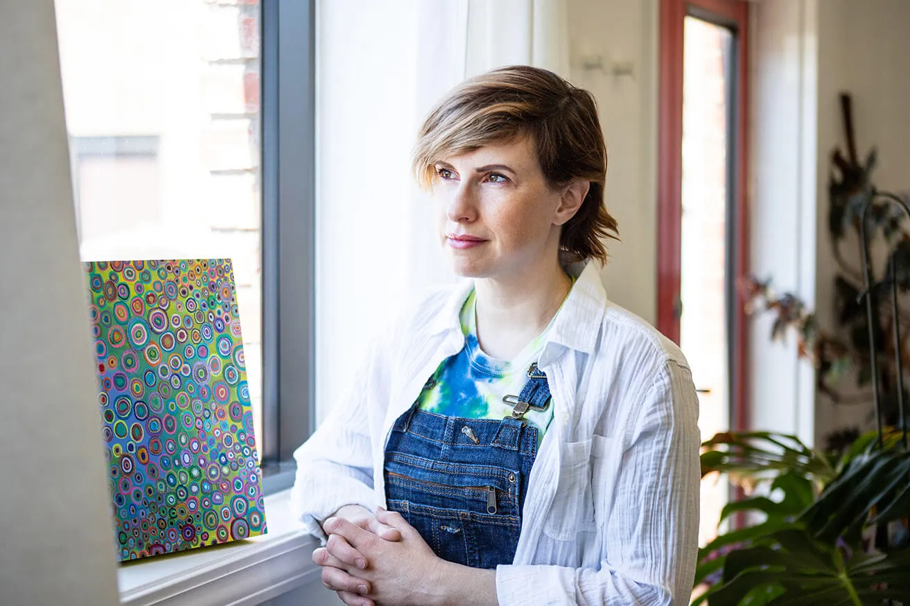 Find Artistic Inspiration. - myheartcreative Artist Sara Cowan gazes out a window at the myheartcreative studio while standing next to one of her pieces.