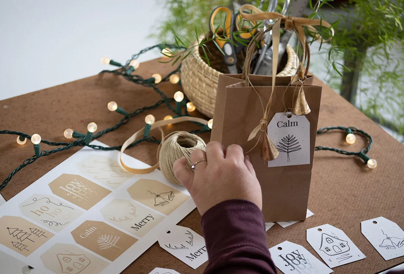 2022 Free Christmas Gift Tag Printables - myheartcreative A woman typing a bow on a Christmas gift bag, complete with printable gift tags created with graphic design OKC elements.