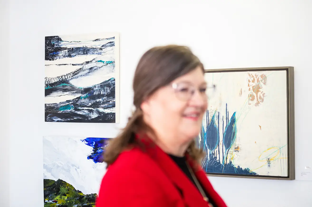Artist Deborah Burian walks around the myheartcreative studio and observes several artworks hanging on the walls. 