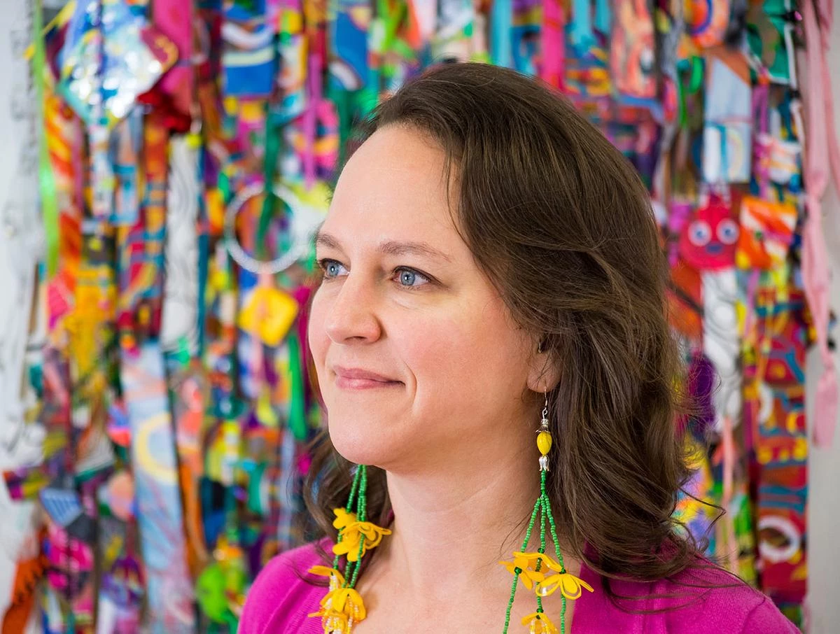 A Vision of Whimsy - myheartcreative Artist Bianca Roland stands in front of a mixed-media piece wearing handmade earrings.