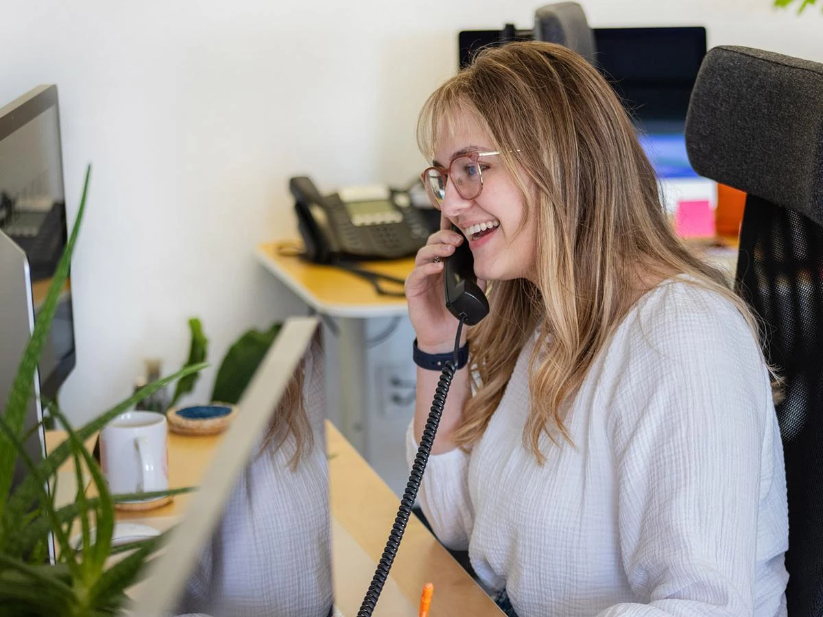A young woman talking to a client through the office phone. 
