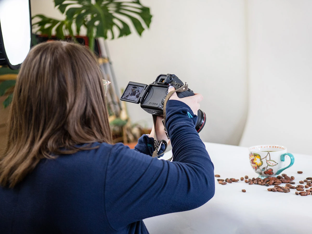 2023 Reflections & 2024 Projections - myheartcreative A female photographer taking a photo of a coffee cup with cocoa beans scattered around it.