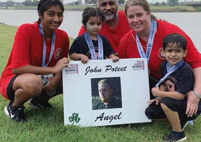 Amy, Sam, and their three children smile with a memorial sign after the Miles Against Melanoma race.