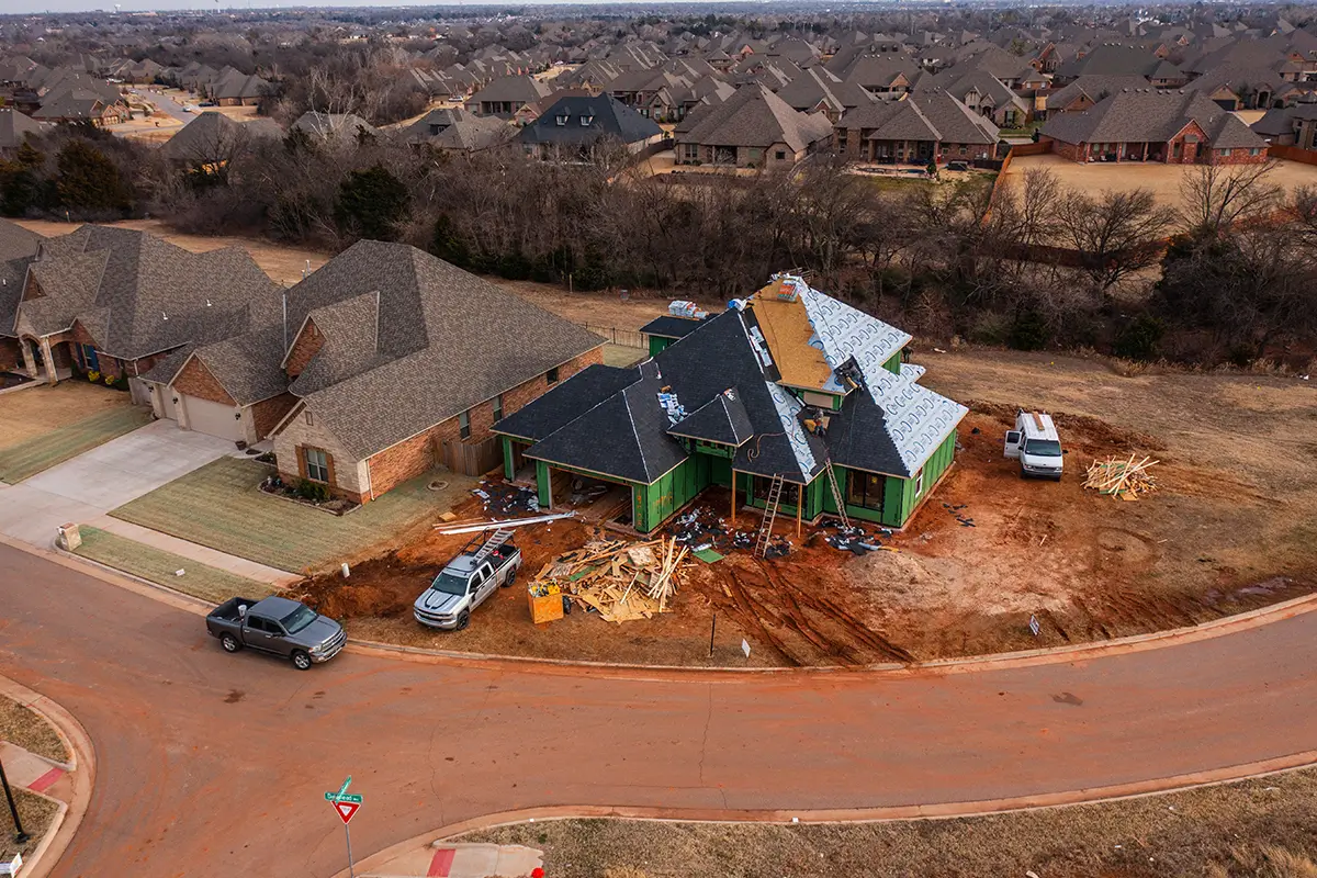 Why Invest in Drone Photography Services? - myheartcreative Aerial drone view of a residential home under construction in an Oklahoma City neighborhood, showing roofing installation, work trucks, and surrounding suburban houses