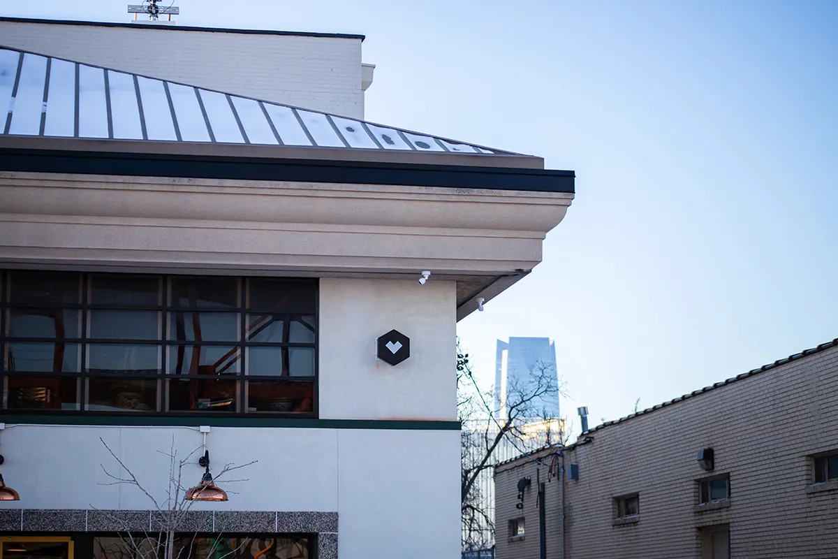 Modern commercial building exterior in downtown Oklahoma City with large industrial windows, rooftop metal awning, and urban skyline in the background.